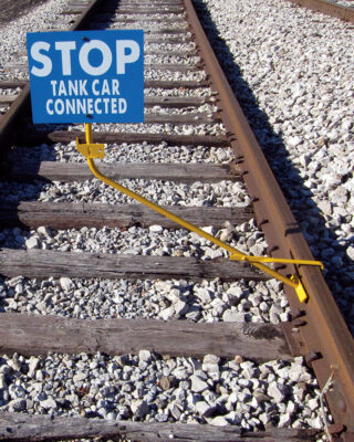 yellow clamp staff attached to rail road tracks displays a stop sign