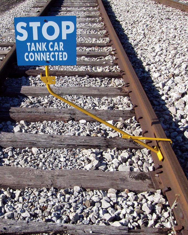 yellow clamp staff attached to rail road tracks displays a stop sign