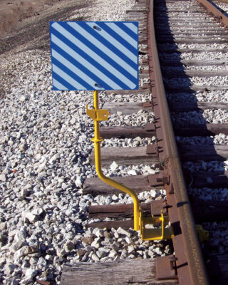 Yellow staff with hinge design mounting a signal flag to rail road tracks