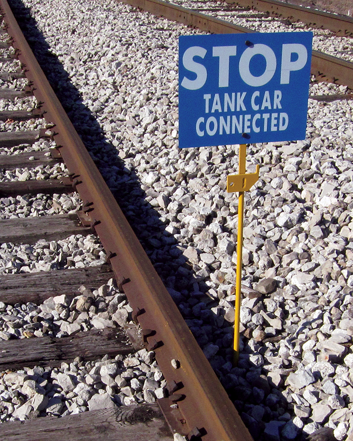 The Spiked Hinged Staff is installed alongside a railroad track with a blue sign that reads: STOP TANK CAR CONNECTED