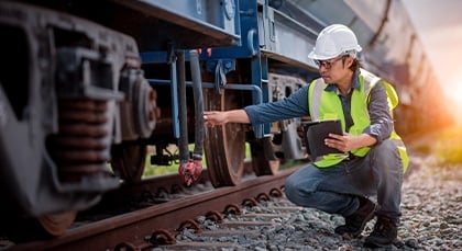 A railroad technician kneels to examine a train car wheel